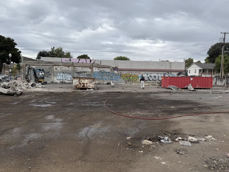 Commercial site part way through demolition with the tagged perimeter walls still up and roll-off bins staged on the slab