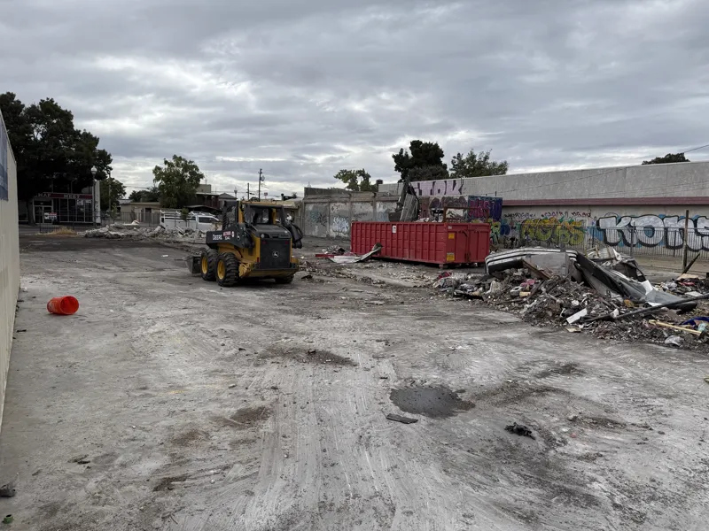 Skid steer working the last of the demolition debris into a roll-off bin on a cleared commercial lot