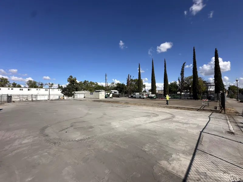 Wide view of the cleared commercial lot with the slab intact and the site fence still up