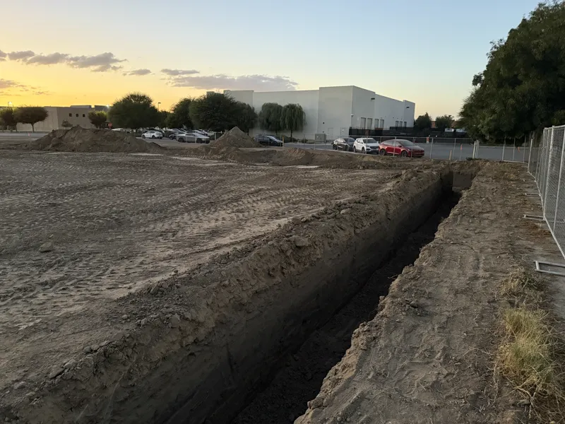 Long footing trench run out along the edge of a commercial pad at dusk with the building beyond