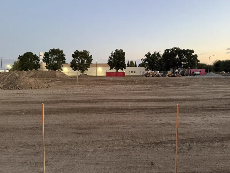 Graded commercial building pad at dusk with grade stakes set and the spoil heaps behind