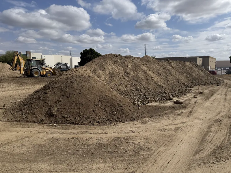 Backhoe working a long soil stockpile on a commercial pad being prepared for construction
