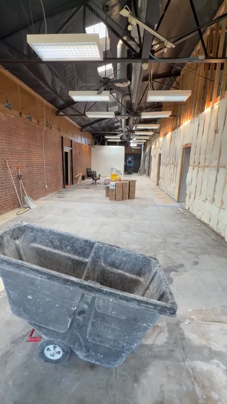 Walkthrough of an open commercial shell with exposed brick walls, an open ceiling with new ductwork and lighting, and floor protection down