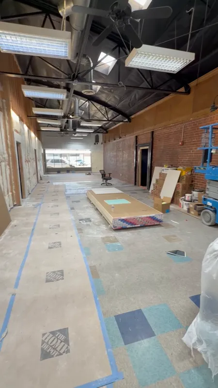 Open commercial ceiling with new ductwork, conduit and light fixtures run above an exposed brick wall