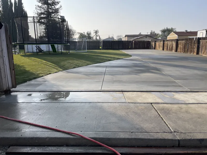 Cured concrete drive and slab washed down, curving around the turf lawn to the gate