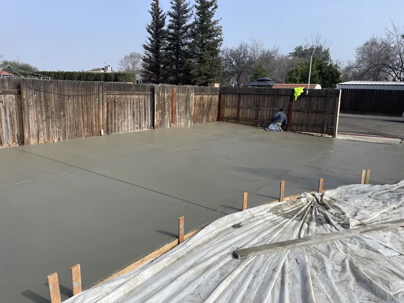Finisher working the edge of a freshly poured concrete slab run wall to wall across a back yard