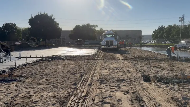 Machine working a large concrete pour on a commercial site with the building beyond