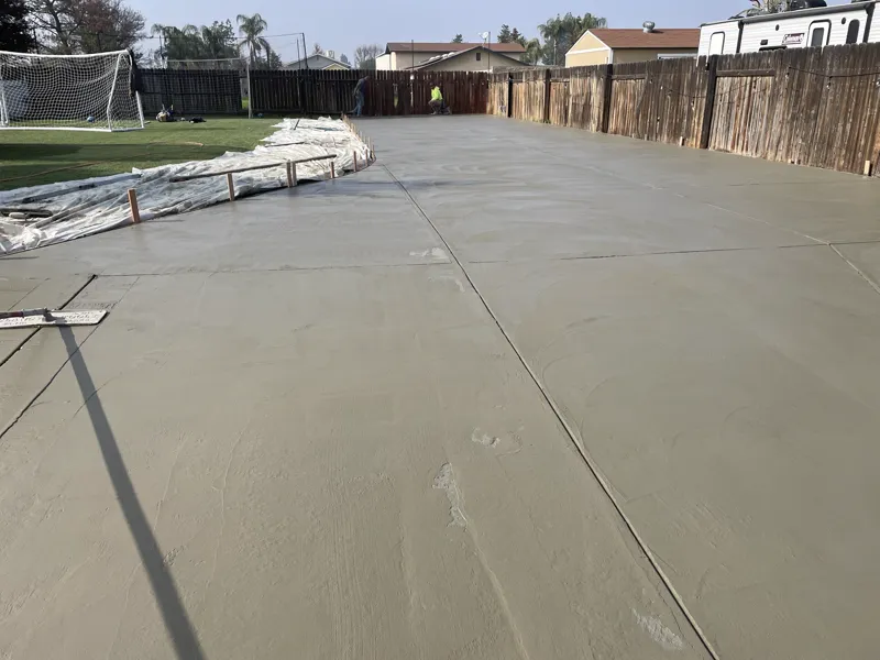 Wide freshly finished concrete slab alongside the lawn with the forms still in place