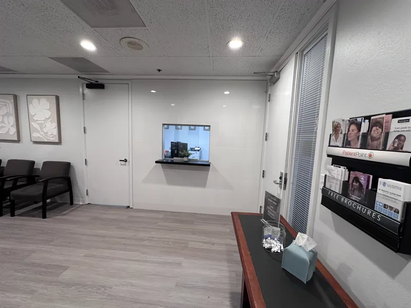 Finished reception transaction window with a stone sill, new doors and a wall-mounted brochure rack in a dermatology clinic