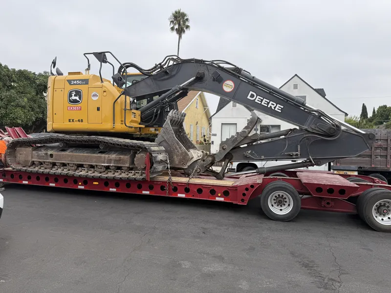John Deere 245G LC excavator chained down on a lowboy trailer ready to leave a residential demolition site