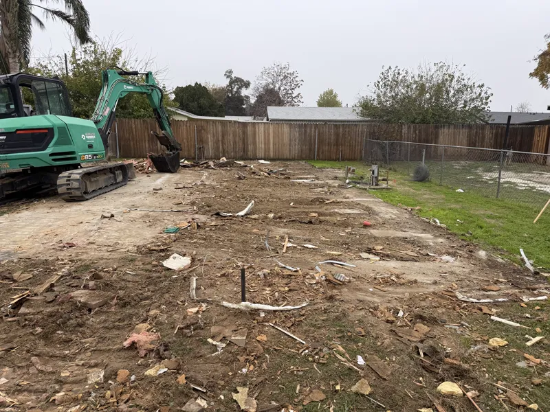Compact excavator clearing the last debris off the pad after a mobile home was removed from a back yard