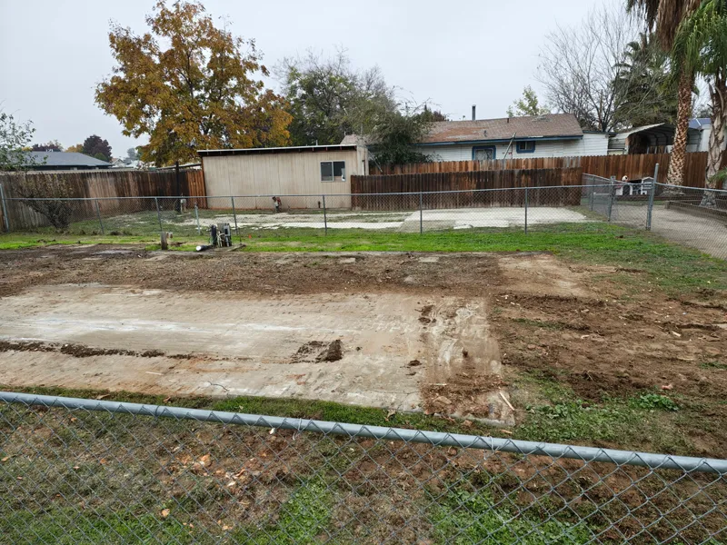 Back yard left graded and clear after a mobile home removal, with the slab swept and the lawn edge intact