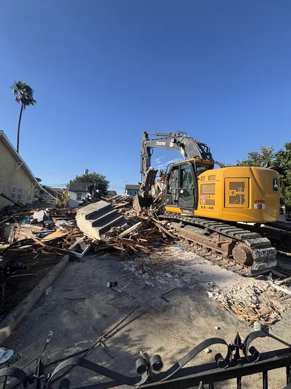 Excavator working down the last standing section of a mobile home against a clear sky