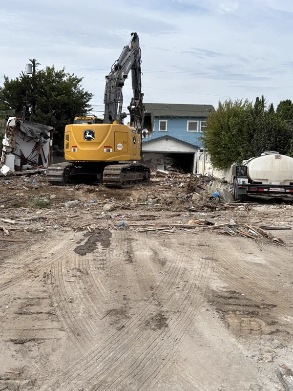Excavator pulling a mobile home apart, with the wall panels and framing dropping onto the pad