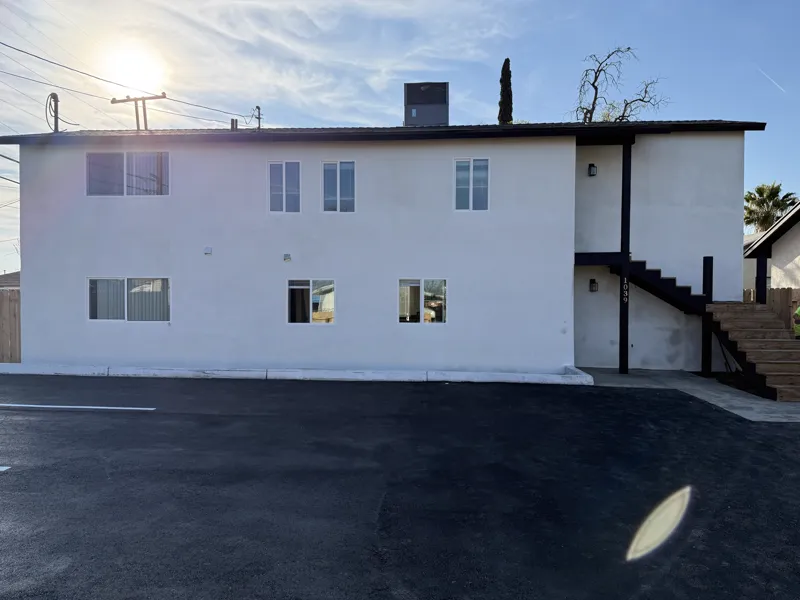 Finished apartment building in white stucco with black fascia, seen across the new asphalt parking lot