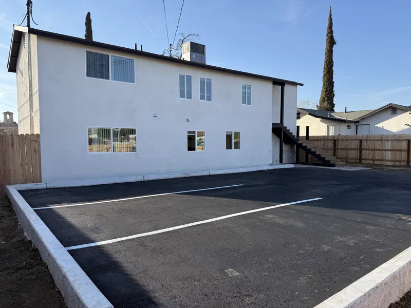 Newly paved and striped asphalt parking lot with fresh concrete curbing alongside the finished building