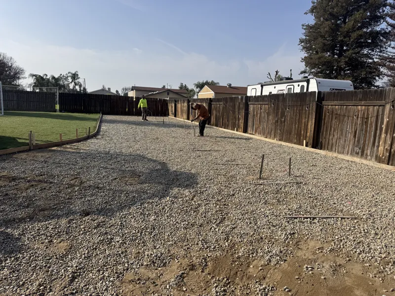 Wide view of the formed RV pad running the length of the fence line, base rock placed and screeded