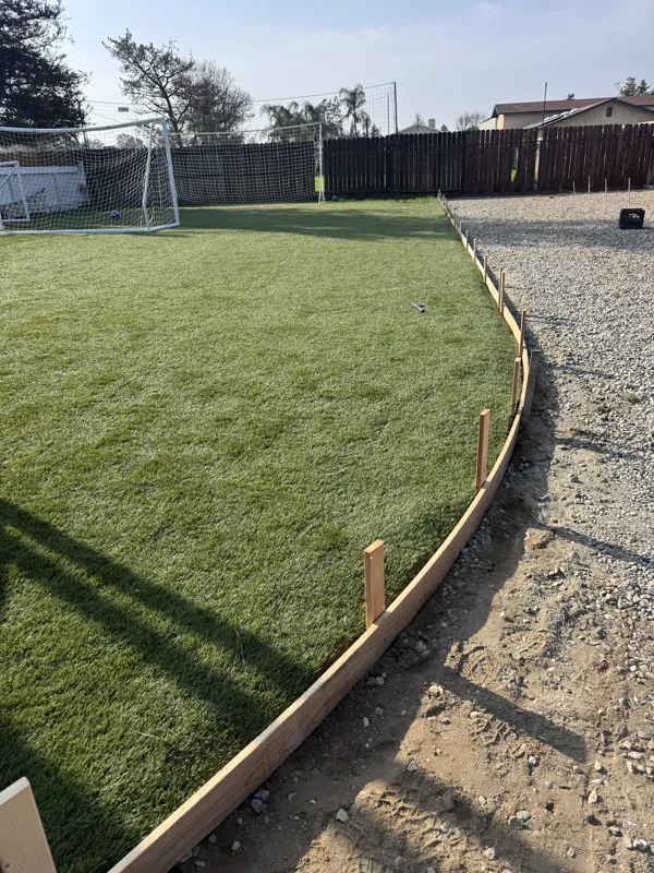 Timber form holding a clean edge between the artificial turf lawn and the new base rock