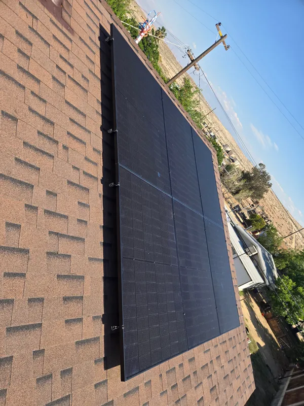 Black solar panels installed along the edge of a composition shingle roof against a clear sky