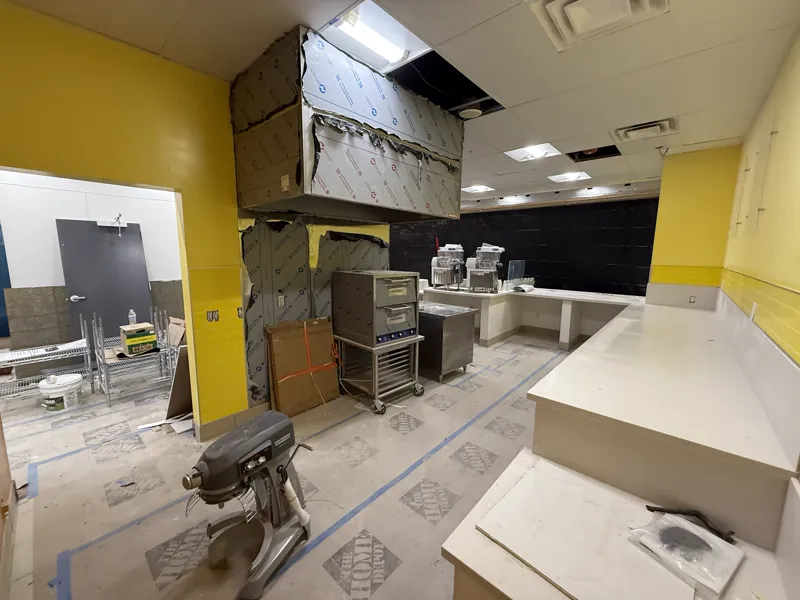 New exhaust hood boxed out and hung over the bake line with yellow tile wainscot and the counter run behind it