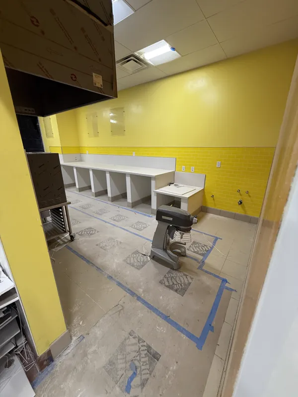 Service counter millwork set and capped with quartz against new yellow wall tile, with the floor still masked and taped