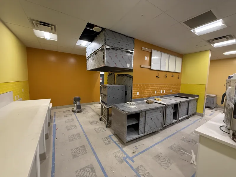 Stainless steel prep line still wrapped, a new exhaust hood hung above it and fresh orange and yellow tile on the back wall